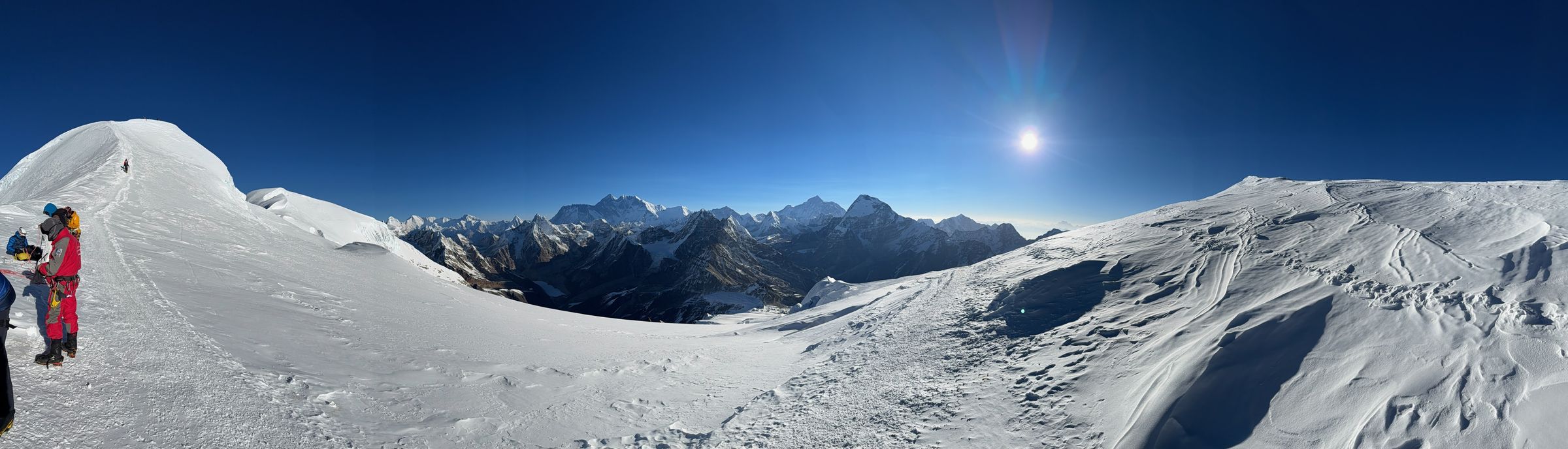 Summit panorama, Mera Peak, April 2026 – climbers on the ridge with the Khumbu Himalayan range visible to the horizon.